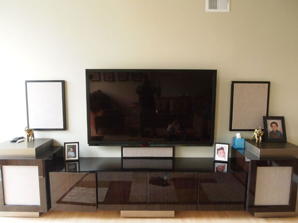 A custom lacquered media console with fabric-covered speaker panels either side of the TV
